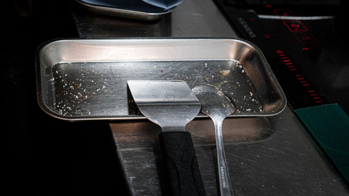Herramientas de cocina: paleta para la carne, cuchara para la mantequilla, sobre una bandeja de metal.