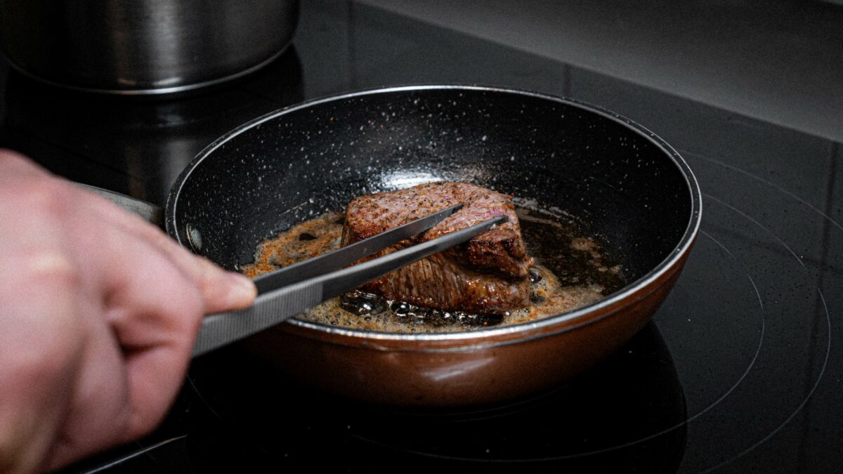 Chef manejando con pinzas de acero el solomillo en la sartén.