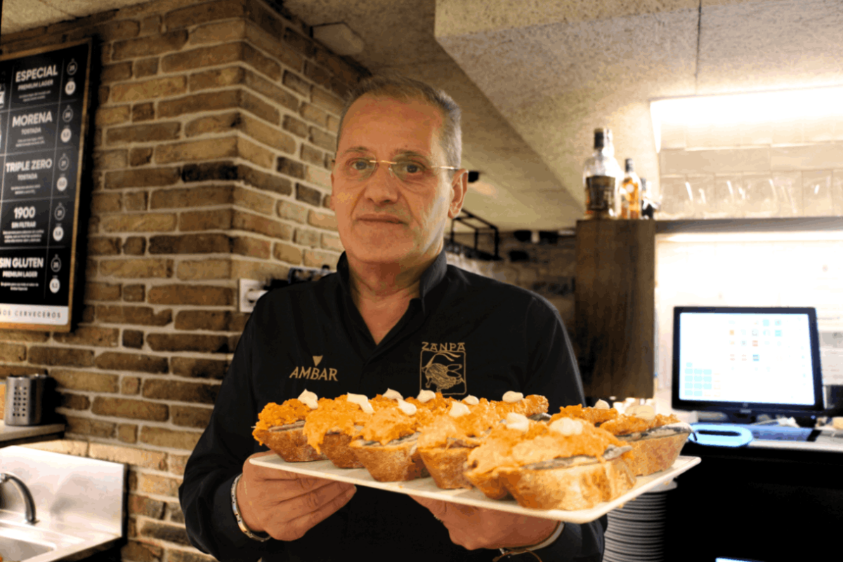 José, camarero del bar Zanpa, mira a cámara mientras sostiene una bandeja repleta de pinchos.
