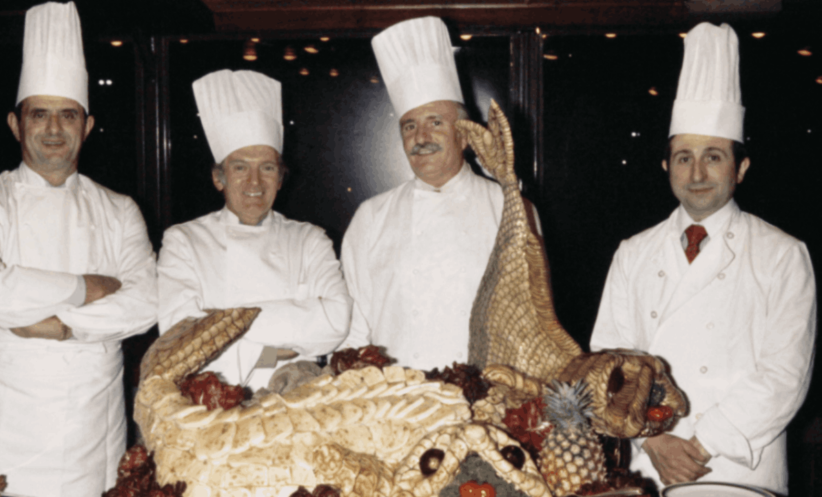 Fotografía de cuatro chefs con uniforme blanco y gorros altos.